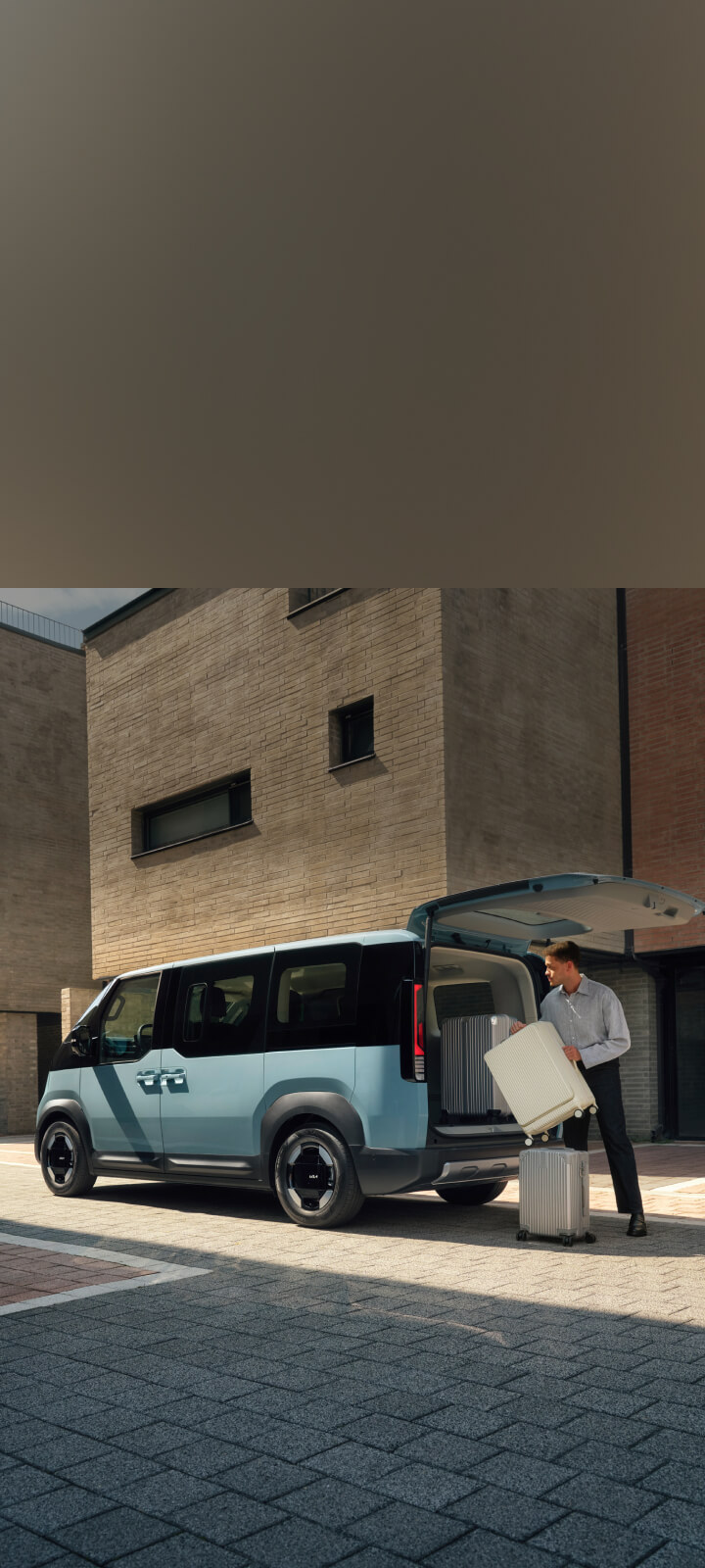 Der Kia PV5 Passenger steht vor einem Waschsalon, die Heckklappe ist geöffnet – Wäsche wird gerade ein- und ausgeladen.